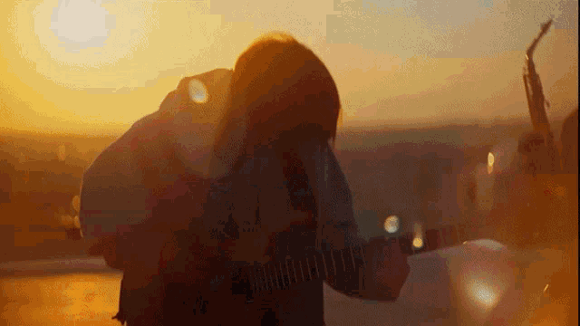 a person is playing a guitar in front of a sunset .