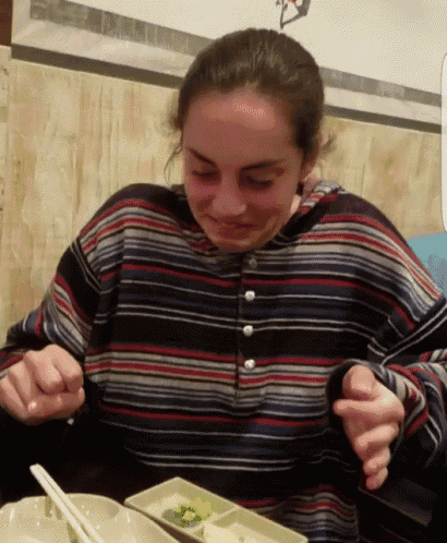 a woman wearing a striped shirt is sitting at a table with chopsticks