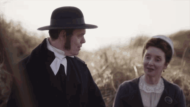 a man in a black hat stands next to a woman in a white shirt