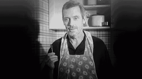 a black and white photo of a man wearing an apron and holding a spoon .