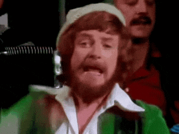 a man with a beard is wearing a green jacket and hat .