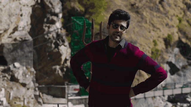 a man wearing glasses and a red sweater is standing in front of a mountain