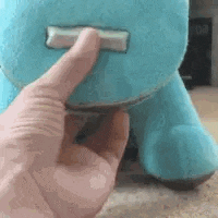 a person is holding a blue stuffed animal with their thumb .