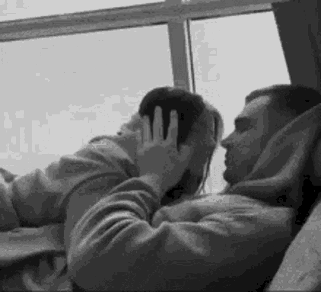 a black and white photo of a man and a woman kissing .