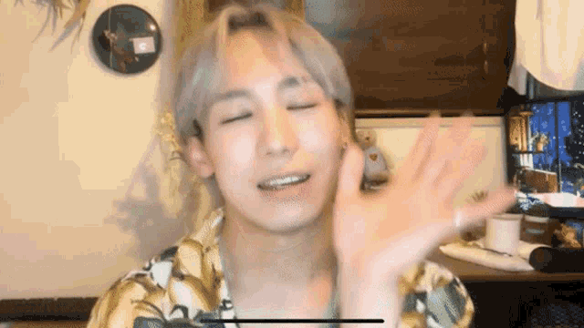 a young man in a floral shirt is waving his hand in front of a tv .