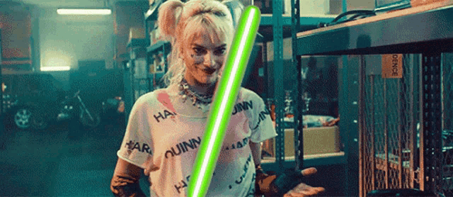 a woman in a harley quinn shirt is holding a green light saber in a garage .