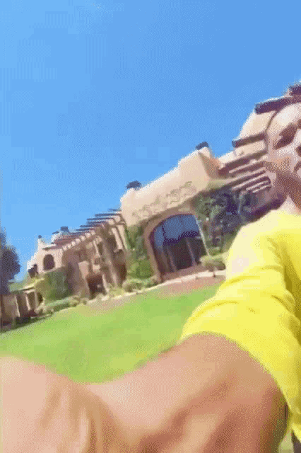 a man in a yellow shirt is taking a selfie in front of a house