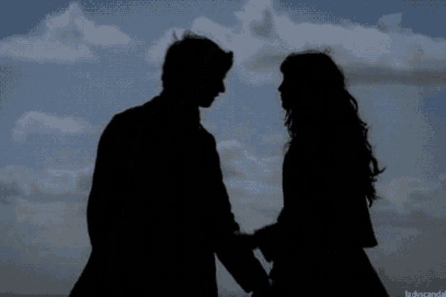 a silhouette of a man and woman kissing in front of a blue sky with clouds