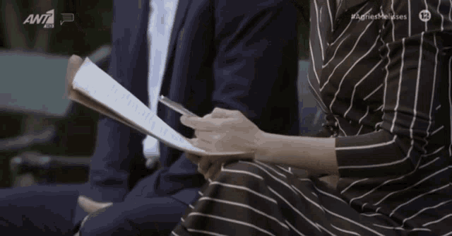 a woman in a striped dress is holding a piece of paper in front of a tv screen that says ant7
