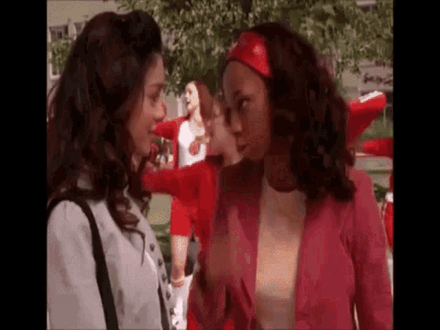two women are standing next to each other and talking to each other in a park .