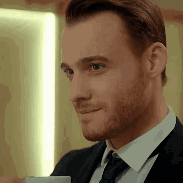 a man in a suit and tie is smiling and holding a cup of coffee