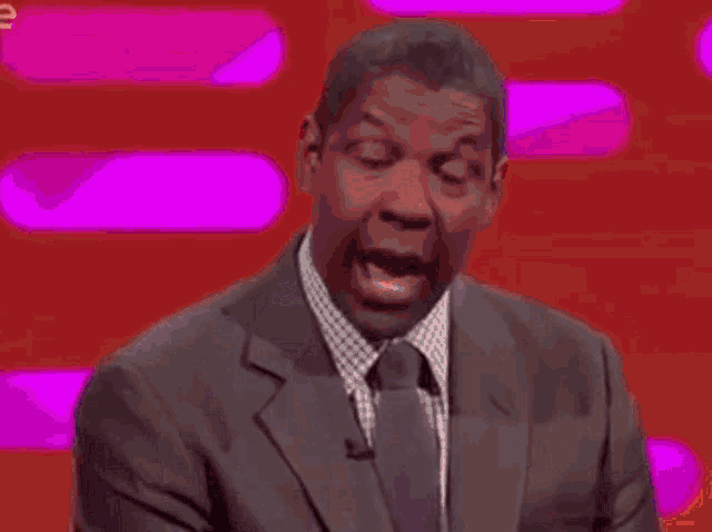 a man in a suit is covering his mouth with his hand while standing in front of a television .