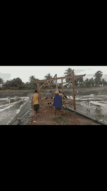 a group of men are working on a wooden structure in front of a pond .