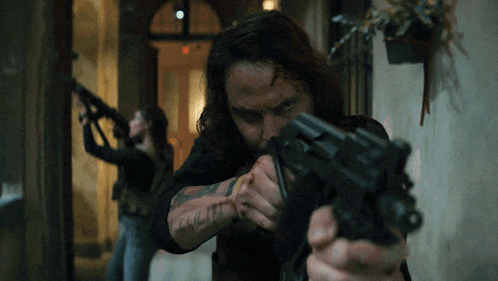a man with a tattoo on his arm is pointing a gun at another man