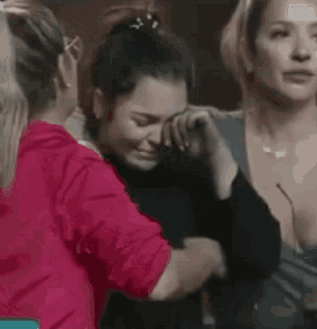 a group of women are hugging each other in a room and one of them is crying .