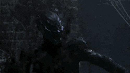a man in a black suit is standing in the dark with his arms outstretched