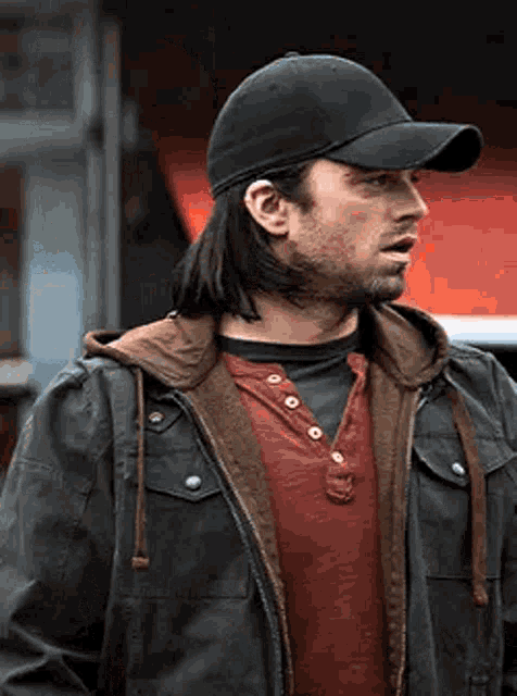 a man wearing a baseball cap and a jacket is standing in front of a red building .