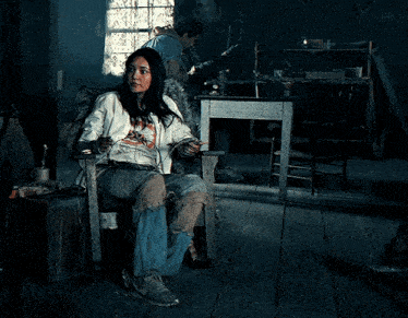 a woman is sitting in a chair in a dark room with a man in the background