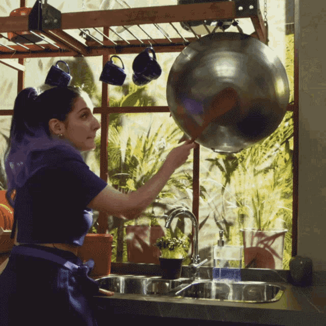 a woman with purple hair is cleaning a pot in a kitchen