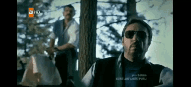 a man wearing sunglasses stands in front of a tv screen that says ahd