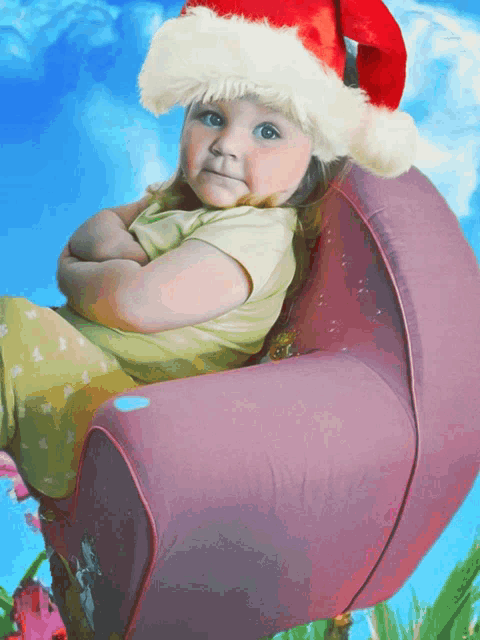 a little girl wearing a santa hat is sitting in a pink chair