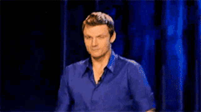 a man in a blue shirt is sitting in front of a black curtain
