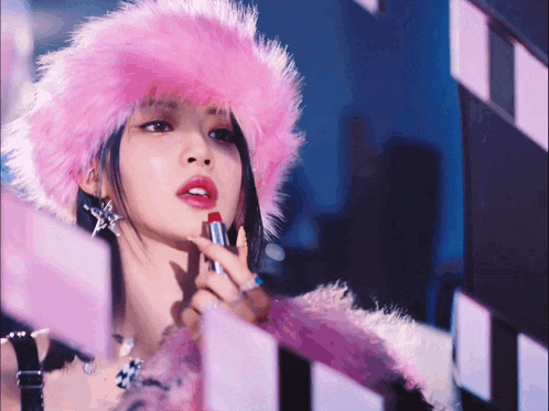 a woman wearing a pink furry hat is applying lipstick
