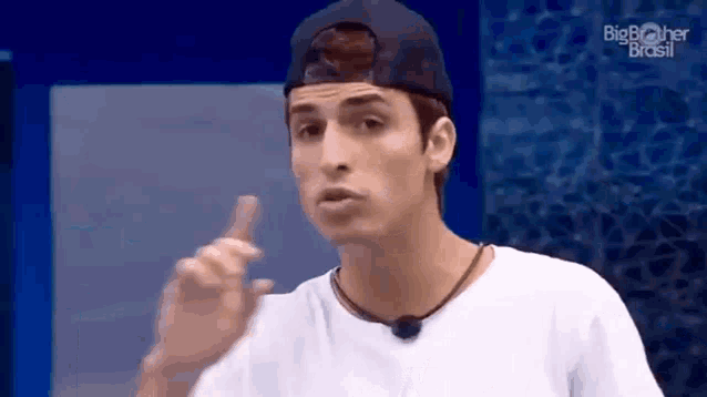 a young man wearing a baseball cap and a white shirt is making a funny face .