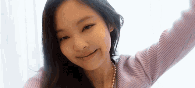 a close up of a young woman wearing a purple sweater and pearls .