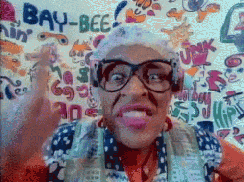 a woman wearing glasses and headphones is standing in front of a wall that says bay-bee on it