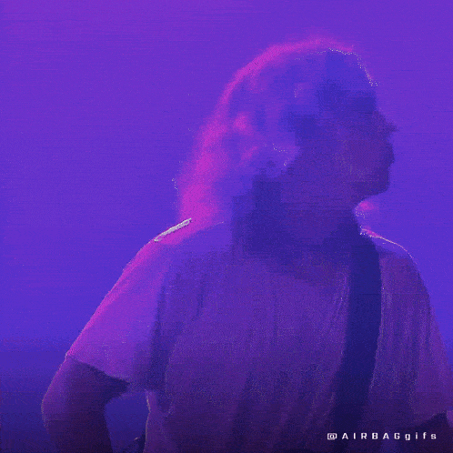 a man in a white shirt is playing a guitar on a stage with purple lights behind him .
