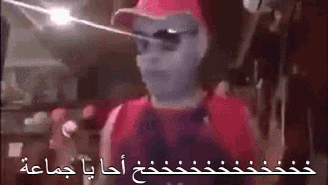 a man wearing a mask and sunglasses is standing in a room with arabic writing on the bottom .