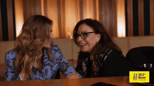 two women are sitting at a table with a sign that says 101.3