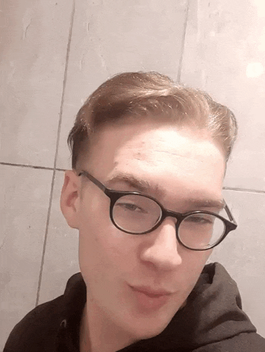 a young man wearing glasses and a black hoodie poses for a picture