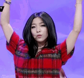 a woman wearing a red plaid shirt holds her arms in the air