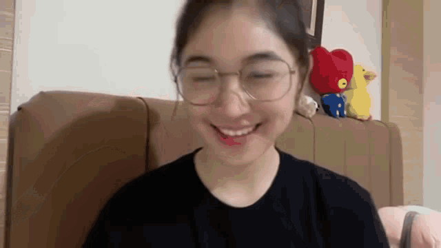 a woman wearing glasses is smiling with her eyes closed while sitting on a couch .
