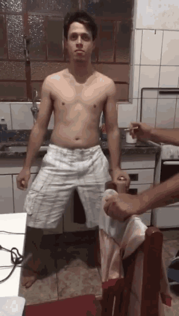 a shirtless man standing in a kitchen holding a can of beer