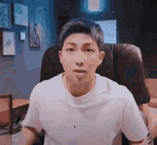 a man in a white t-shirt is sitting in a chair and making a funny face .