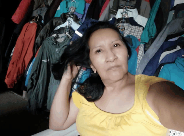 a woman in a yellow tank top is standing in front of a wall of clothes