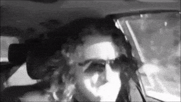 a woman wearing sunglasses is driving a car .