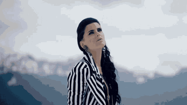 a woman in a black and white striped shirt stands in front of mountains