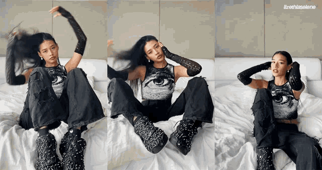 a woman is sitting on a bed wearing black pants and a black top with an eye on it