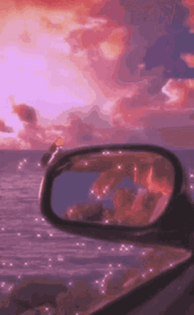 the rear view mirror of a car shows a reflection of a sunset over the ocean .
