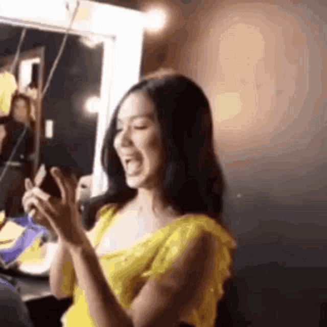 a woman in a yellow dress is clapping her hands in front of a mirror in a room .