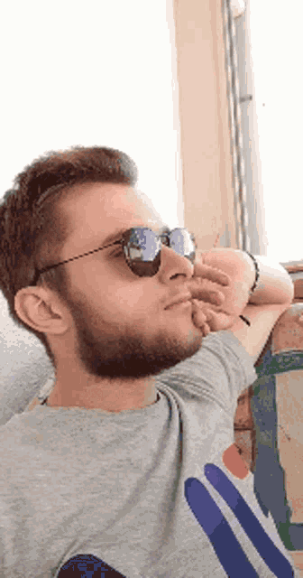 a man with a beard wearing sunglasses and a gray shirt with a blue circle on it