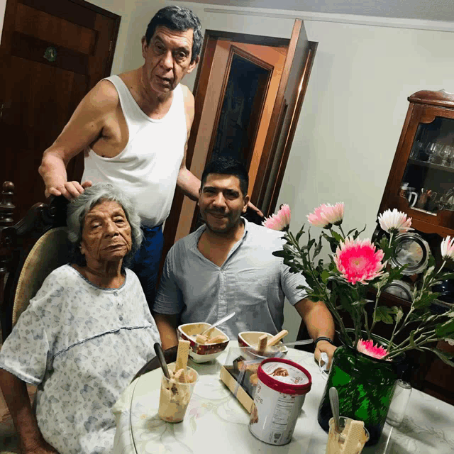two men and an elderly woman sit at a table with a container of ice cream