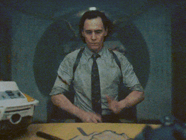 a man in a suit and tie is sitting at a table with his hands in the air and says great !