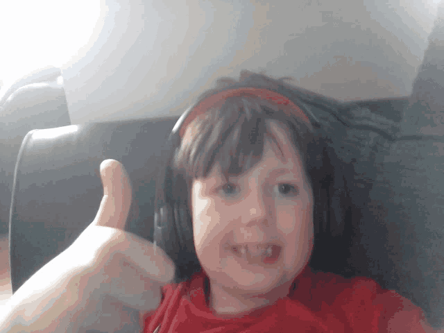a young boy wearing headphones gives a thumbs up sign