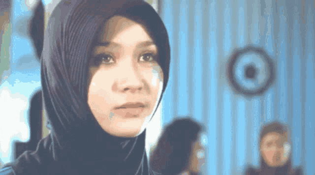 a woman wearing a hijab looks at the camera with a target in the background