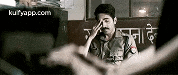 a man in a police uniform is sitting in a room with his hand on his forehead .